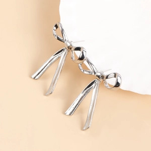 Macro detail of silver bow earrings with long metal ribbons on aesthetic background