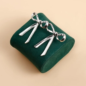 Elegant silver bow knot stud earrings with polished metallic finish on green display