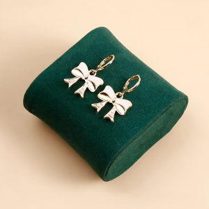 Detail of gold bow earrings with white enamel finish on dark green velvet padding