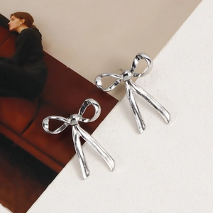 Close-up of elegant silver bow-knot earrings on a minimalist textured fashion background
