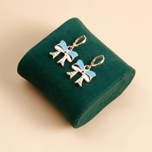 Detailed macro view of light blue and white enamel bow earrings on green velvet