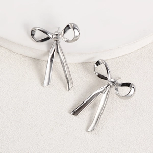 Detailed view of polished silver bow stud earrings on a clean white display stand