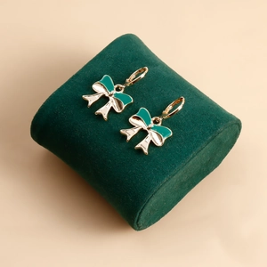 Detail of elegant gold hoop earrings with green and white enamel bow design on velvet