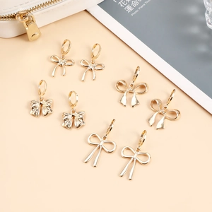 Vue à plat de quatre modèles de boucles d'oreilles nœuds dorés sur un fond beige chaud