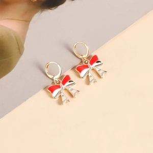Close-up of golden hoop earrings featuring red and white enamel bow charms on magazine background