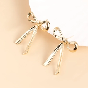 Detail of elegant gold bow earrings with long ribbons on a white display stand