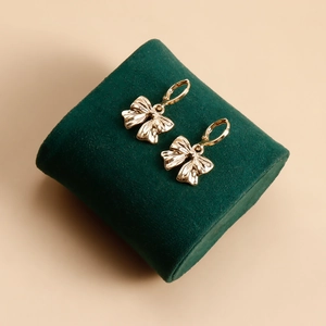 Vue macro de boucles d'oreilles nœuds dorés avec fermoirs sur support en velours vert