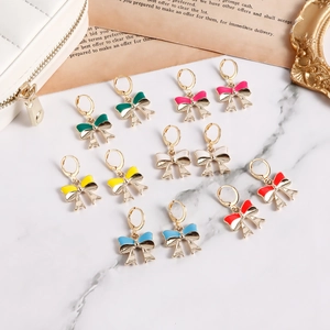 Detailed close-up of colorful enamel bow earrings in six vibrant shades on a marble base