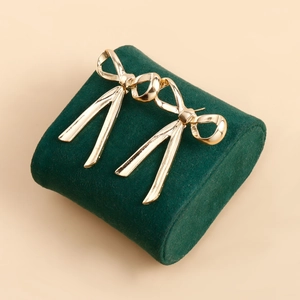 Macro detail of golden bow earrings with long tassels on a green velvet stand