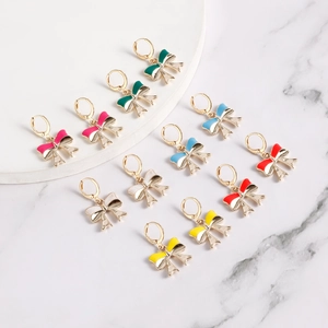 Close-up of six colorful enamel bow earrings on white marble background with gold hooks
