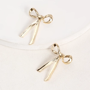 Close-up of golden bow-knot earrings with hanging ribbons on a minimalist white stand