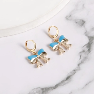 Close-up of golden bow earrings with bright blue enamel detail on a marble surface