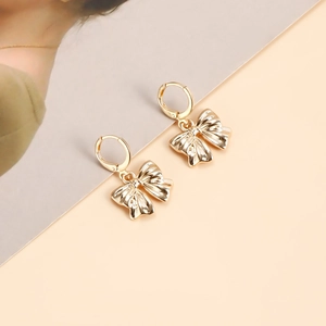 Détail de boucles d'oreilles nœuds dorés avec cercles en métal texturé sur fond minimaliste