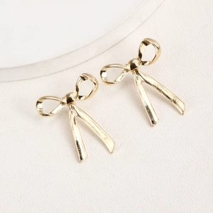 Close-up of polished gold bow stud earrings on a minimalist white texture background
