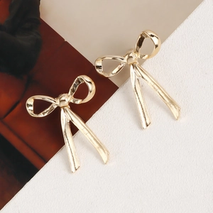 Close-up of golden ribbon bow stud earrings with a polished metallic mirror finish