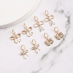 Détails de boucles d'oreilles nœuds dorés aux textures variées sur fond de marbre blanc