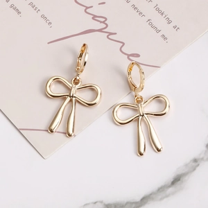 Détail de boucles d'oreilles pendantes à nœud doré sur une carte cadeau rose chic