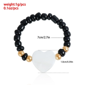 Dettaglio del bracciale elastico con perline nere e ciondolo a cuore bianco