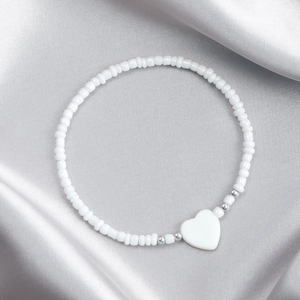 Dettaglio della collana di perline bianche con ciondolo a cuore in madreperla su seta