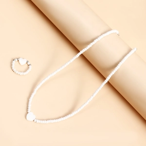 Dettaglio del set di collana e anello di perline bianche con ciondolo a cuore minimalista