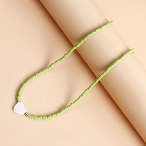 Dettaglio di collana con perline verdi e pendente a cuore bianco con accenti dorati