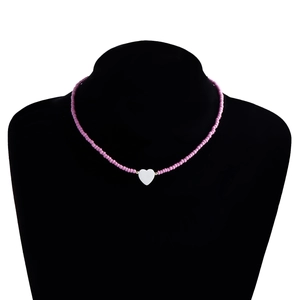 Dettaglio della collana di perline rosa con ciondolo a cuore bianco su busto nero