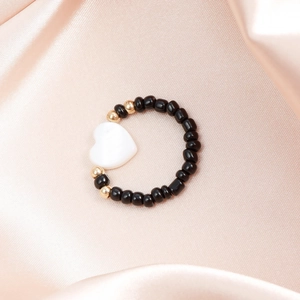 Dettaglio di un anello fatto a mano con perle nere, distanziatori dorati e cuore bianco