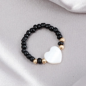 Dettaglio macro di un anello di perline nere con accenti dorati e ciondolo a cuore bianco