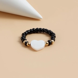 Dettaglio anello di perline nere con accenti dorati e ciondolo a cuore bianco