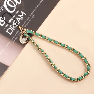 Dettaglio del cinturino per telefono in pelle intrecciata verde e oro con ciondolo luna