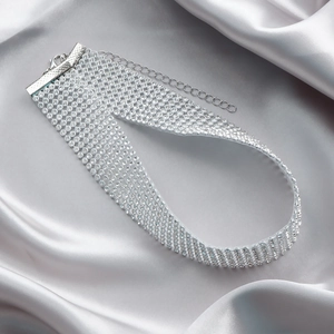 Nahaufnahme von glitzerndem Silber-Strass-Choker mit Karabinerverschluss auf Seide