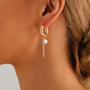 Pendientes de aro dorados con barra larga de metal y cubo de cristal en una modelo