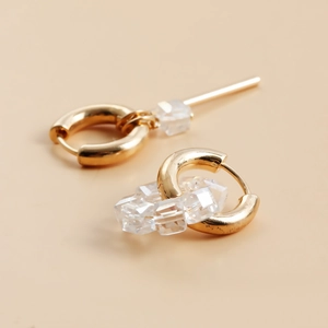 Detalle de pendientes de aro dorados con tres cuentas de cristal tallado transparentes
