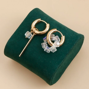 Detalle de pendientes asimétricos dorados con cubos de cristal y una barra de metal fina