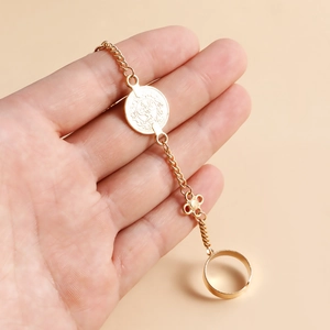 Détail d'un bracelet bague vintage doré avec breloque pièce et pendentif fleur sur main