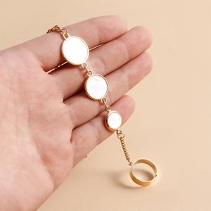 Vue détaillée d'un bracelet de doigt doré avec trois breloques blanches sur une main de femme