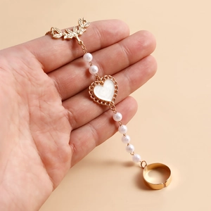 Détail de la gourmette vintage dorée avec perles et pendentif cœur blanc sur main