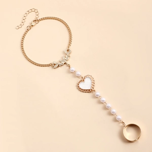 Détail d'un bracelet bague doré avec breloque papillon, cœur blanc et chaîne perlée