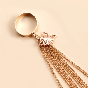 Détail d'une bague papillon dorée ajourée avec de longues chaînes à glands sur fond chaud