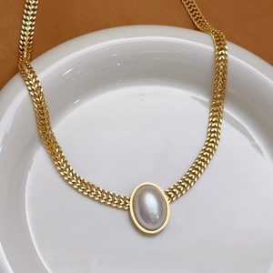 Vintage Goldkette mit großem ovalen Perlenanhänger auf einem weißen Keramikteller