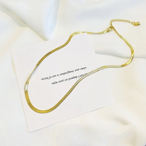 Detail of flat gold snake chain necklace with heart charm and extender on white card