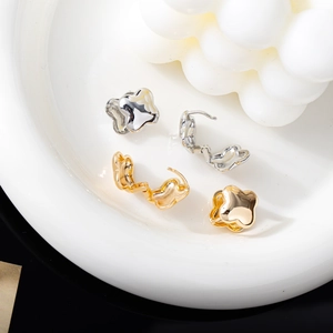 Orecchini a quadrifoglio lucidi in oro e argento su uno sfondo di ceramica bianca pura