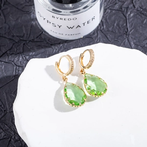 Close-up of teardrop green crystal earrings with gold micro-pave detailing on white marble