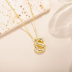 Dettaglio macro di una collana con ciondolo a lettera S dorata con cristalli su pietra