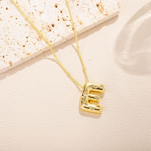 Dettaglio macro della collana con ciondolo lettera E dorata e zirconi su pietra beige