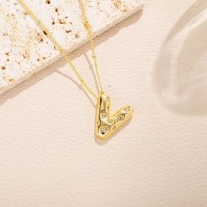 Dettaglio della collana con lettera V dorata e cristalli su una sottile catena a sfere