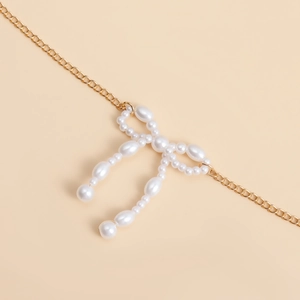 Détail de l'élégante chaîne dorée avec pendentif nœud en perles blanches pour femme