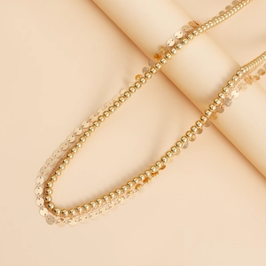 Détail d'une chaîne dorée à plusieurs rangs avec paillettes sur fond minimaliste