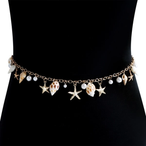 Détail d'une chaîne de taille bohème dorée avec étoile de mer, coquillages et perles