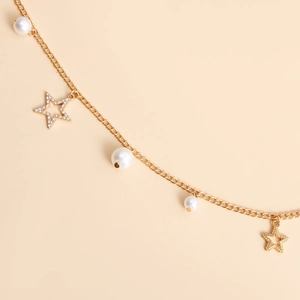 Catena da vita dorata alla moda con perle e ciondoli a stella su sfondo beige
